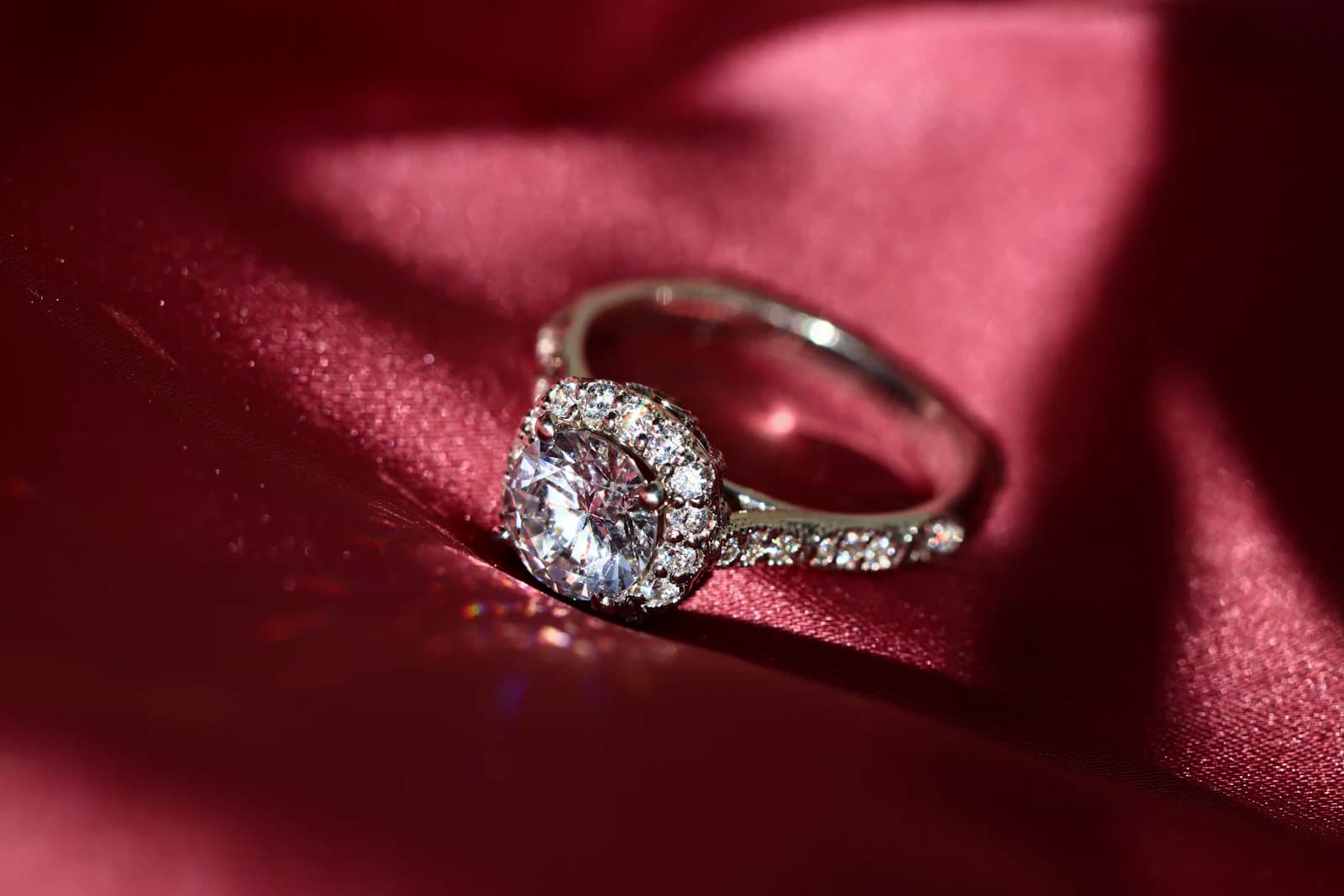 Diamond halo engagement ring resting on deep red satin